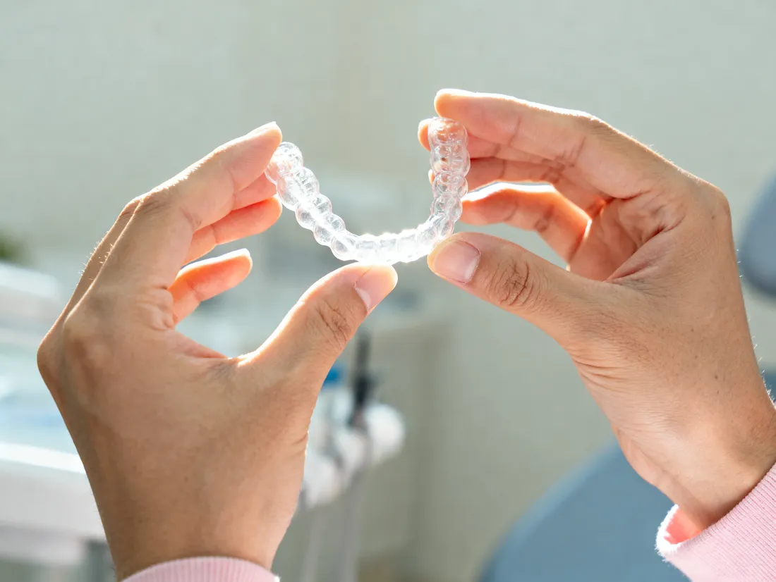 Hands holding a clear dental aligner up to the light